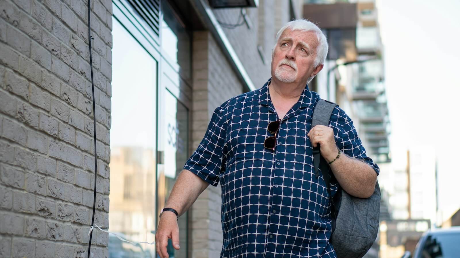 Older man with white hair walking along a city street